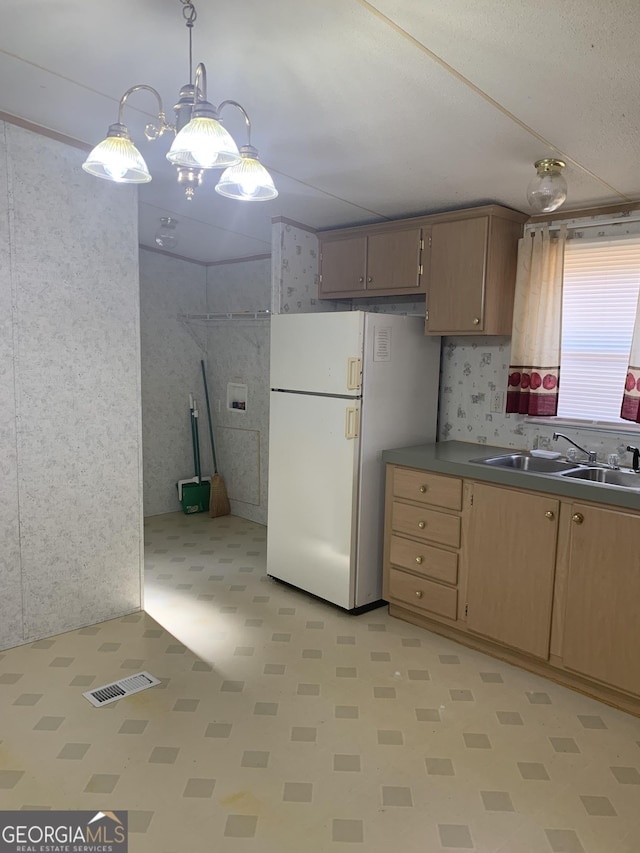 kitchen featuring visible vents, freestanding refrigerator, light floors, a sink, and decorative light fixtures
