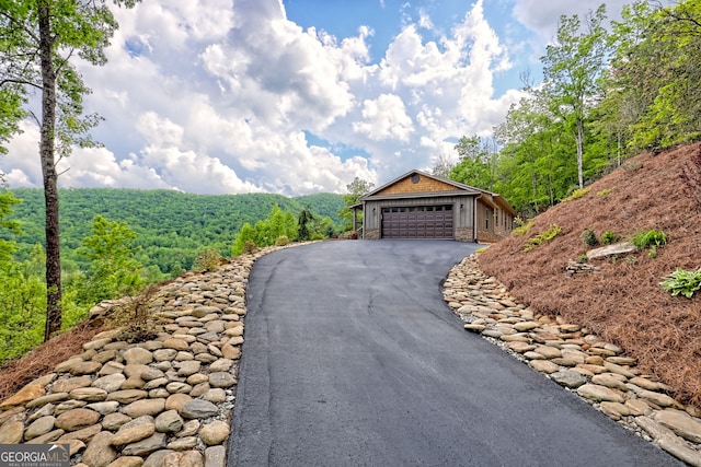 view of front facade with driveway, a forest view, stone siding, and an attached garage
