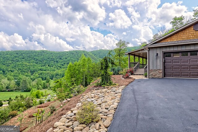 view of side of home featuring board and batten siding, asphalt driveway, a forest view, and a garage