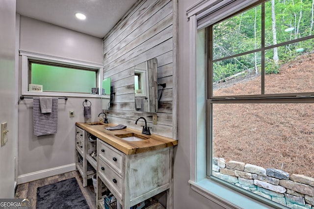 bathroom with wood finished floors, double vanity, baseboards, and recessed lighting