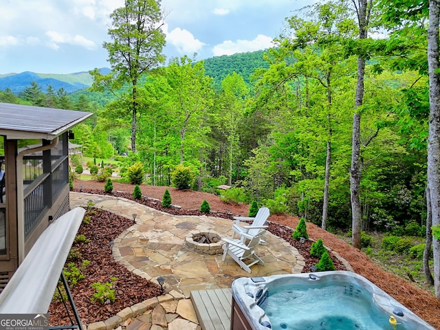 view of patio / terrace featuring a fire pit, a hot tub, a mountain view, and a view of trees
