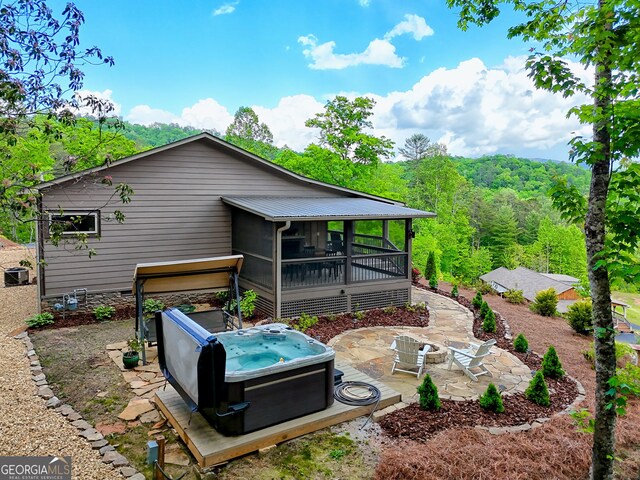 back of house with a hot tub, a patio, a sunroom, and a view of trees