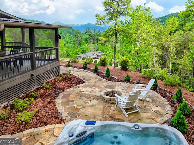 view of yard featuring a patio, an outdoor fire pit, a sunroom, a hot tub, and a mountain view