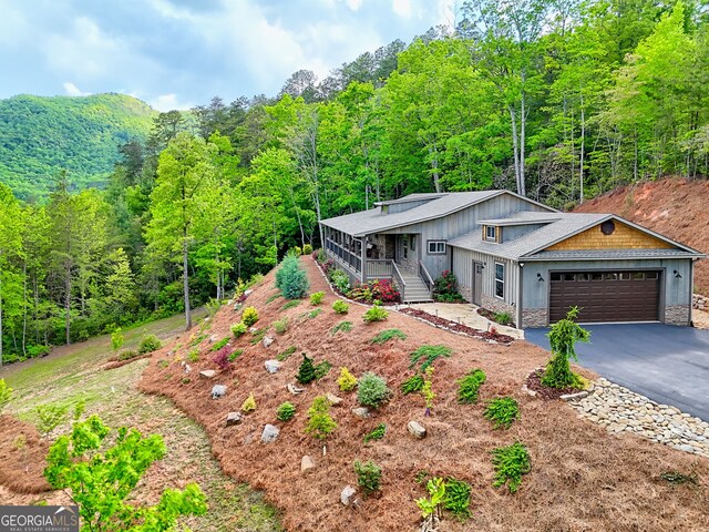 view of front of property with covered porch, stone siding, asphalt driveway, and an attached garage