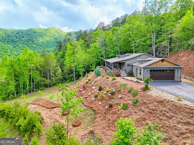 view of front of property with driveway, a wooded view, a garage, and covered porch