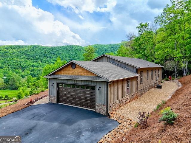 view of front of home with driveway, board and batten siding, roof with shingles, and stone siding