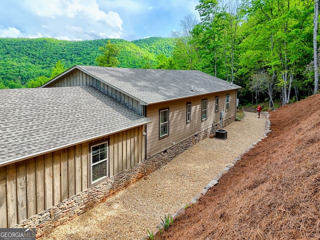 view of side of property featuring roof with shingles, board and batten siding, and a forest view