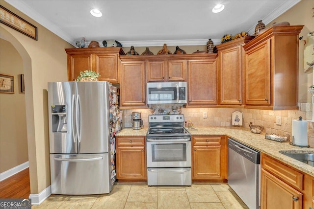 404 Hunts Landing Dr, Kathleen, GA 31047 - kitchen featuring crown molding, appliances with stainless steel finishes, light stone counters, arched walkways, and backsplash