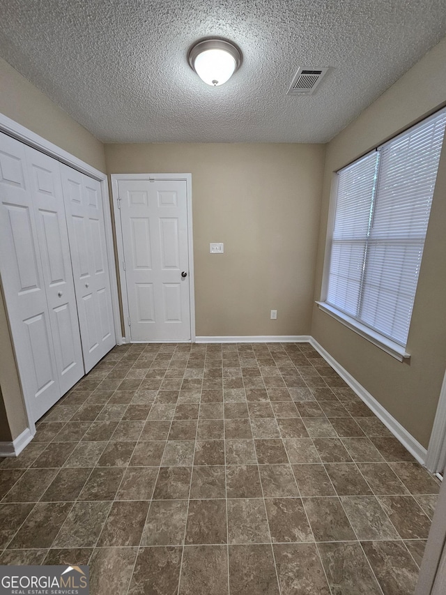 unfurnished bedroom with visible vents, a textured ceiling, baseboards, and a closet