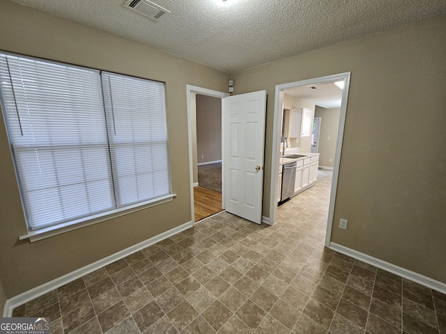 spare room with a sink, baseboards, a textured ceiling, and visible vents