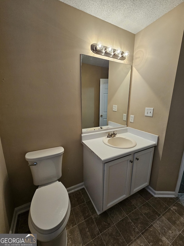 half bath with toilet, a textured ceiling, baseboards, and vanity