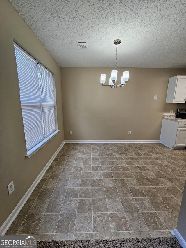 unfurnished dining area featuring baseboards, a textured ceiling, visible vents, and an inviting chandelier