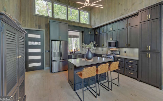 kitchen with a high ceiling, a breakfast bar, light wood finished floors, wood walls, and stainless steel appliances
