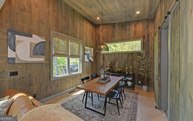dining room with wooden walls, visible vents, a barn door, and a wealth of natural light