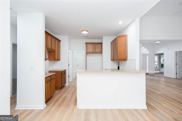 3314 Dilmus Dr, Powder Springs, GA 30127 - kitchen featuring brown cabinetry, light wood-type flooring, a peninsula, light stone counters, and recessed lighting