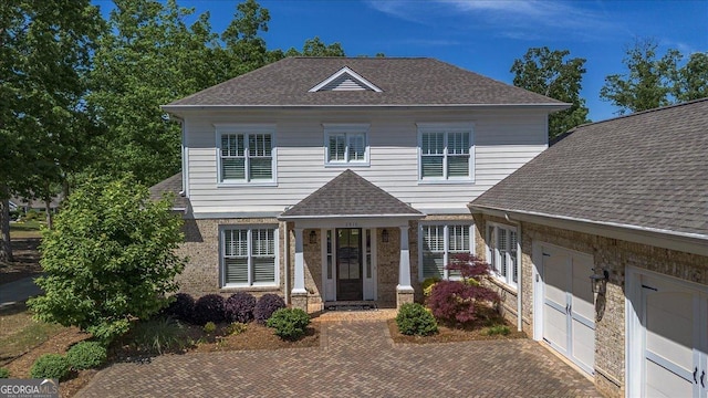 view of front of property with decorative driveway, a shingled roof, and a garage