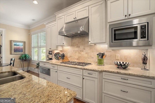 kitchen featuring crown molding, under cabinet range hood, white cabinets, appliances with stainless steel finishes, and backsplash
