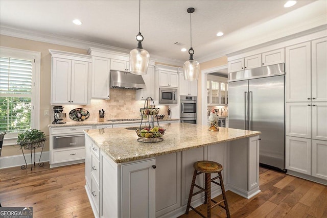 kitchen featuring a warming drawer, hardwood / wood-style flooring, built in appliances, under cabinet range hood, and an island with sink