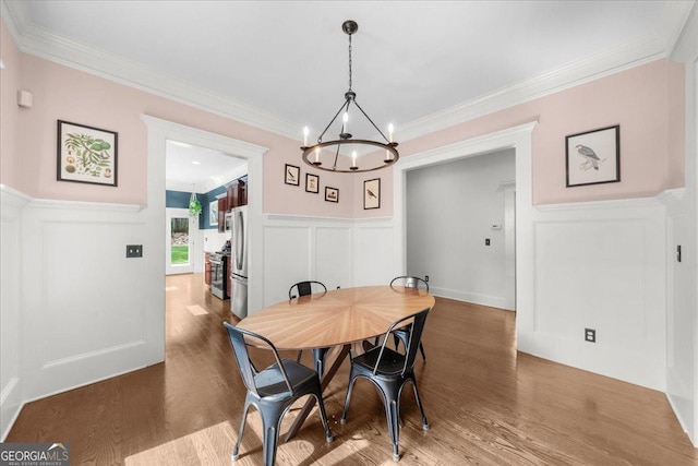 dining area featuring a wainscoted wall, wood finished floors, a chandelier, and a decorative wall