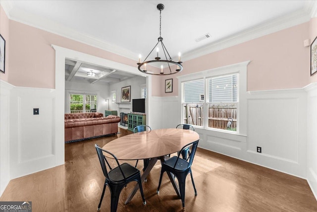 dining space with wood finished floors, coffered ceiling, visible vents, a decorative wall, and a chandelier