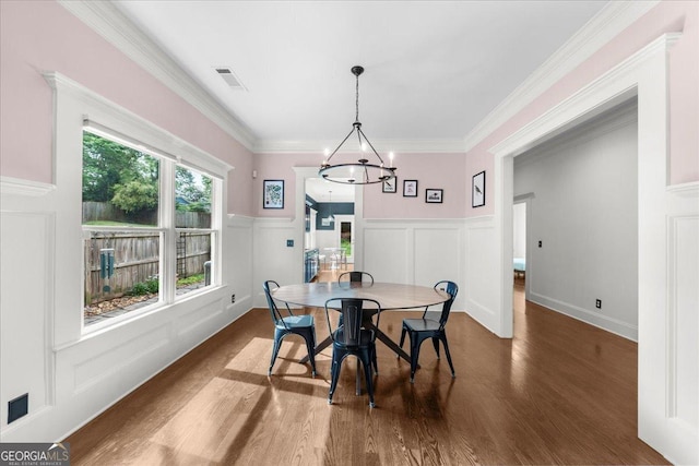 dining space with a decorative wall, wood finished floors, visible vents, an inviting chandelier, and wainscoting
