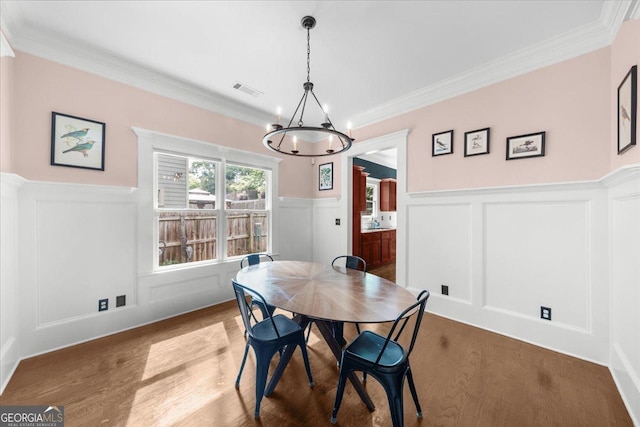 dining area featuring wood finished floors, visible vents, a decorative wall, wainscoting, and a chandelier