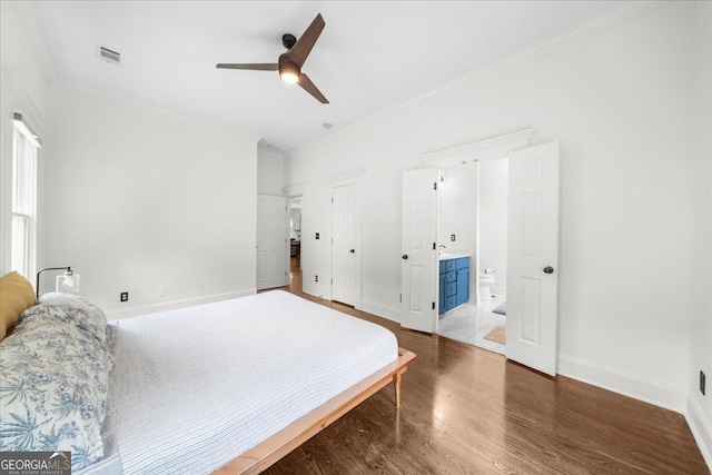 bedroom featuring baseboards, ornamental molding, visible vents, connected bathroom, and wood finished floors