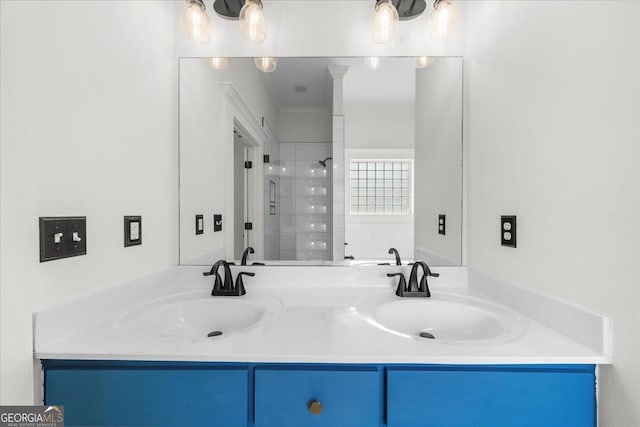 bathroom featuring double vanity, a tile shower, and a sink