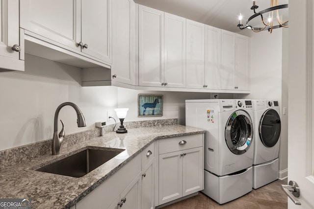 laundry area featuring a sink, washer and clothes dryer, cabinet space, wood finished floors, and a notable chandelier
