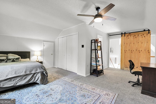 carpeted bedroom featuring a textured ceiling, lofted ceiling, an office area, a barn door, and ceiling fan