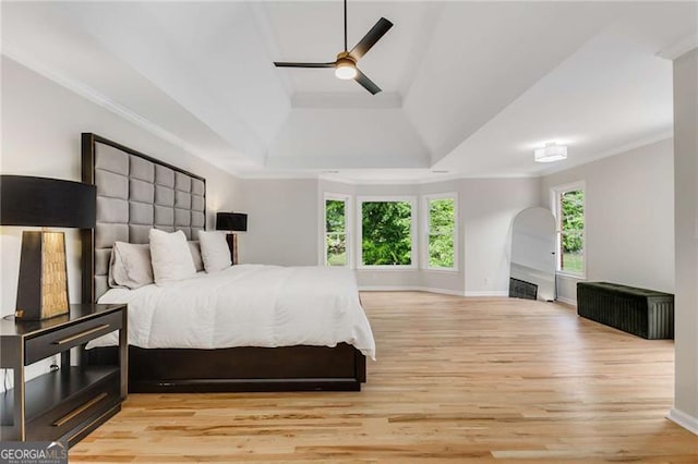 bedroom with crown molding, a raised ceiling, light wood finished floors, and baseboards