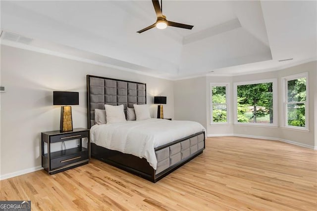 bedroom with multiple windows, a tray ceiling, light wood finished floors, and visible vents