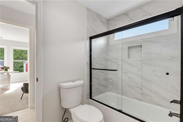 full bathroom featuring plenty of natural light, toilet, and shower / bath combination with glass door