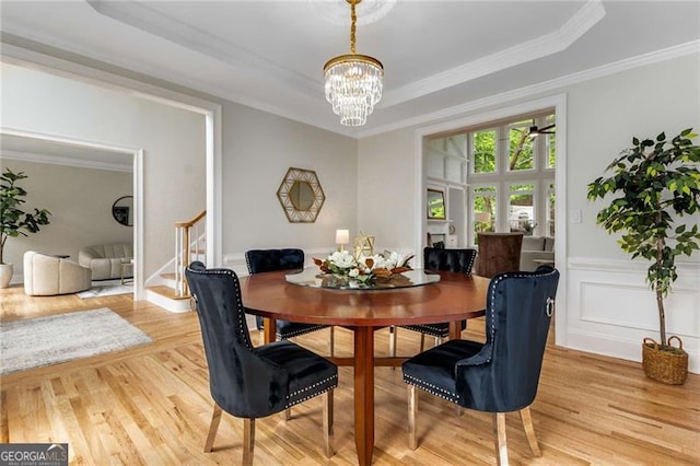 dining room with crown molding, stairway, light wood-type flooring, a tray ceiling, and a notable chandelier