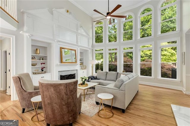 living area with crown molding, ceiling fan, built in shelves, and a towering ceiling