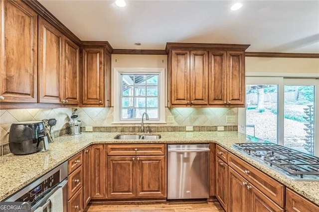 kitchen with ornamental molding, light stone countertops, brown cabinets, a sink, and appliances with stainless steel finishes