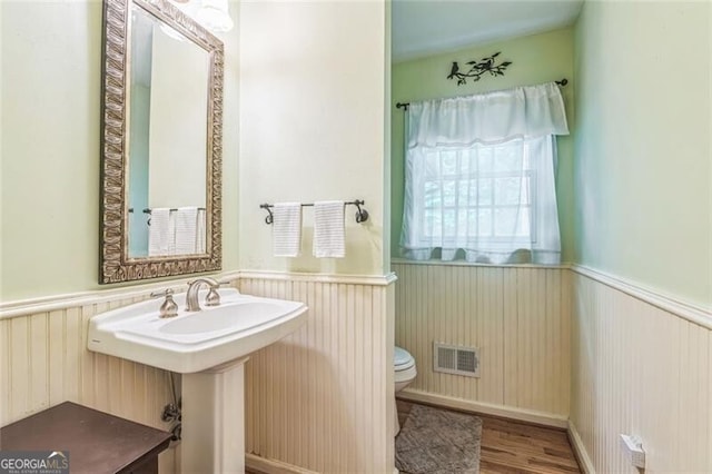 half bathroom with toilet, visible vents, wainscoting, and wood finished floors
