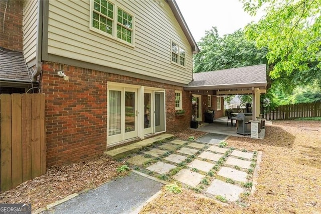 rear view of house with fence, roof with shingles, brick siding, a patio area, and french doors