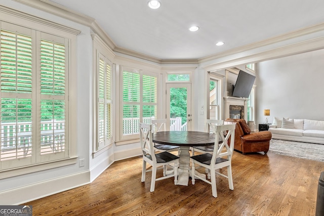 dining space featuring ornamental molding, a glass covered fireplace, wood finished floors, and a wealth of natural light