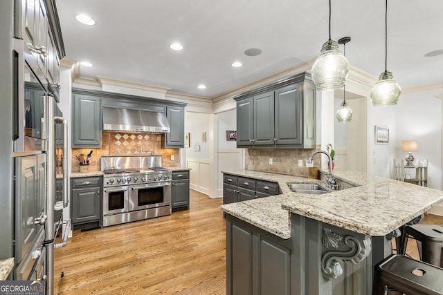kitchen with wall chimney range hood, double oven range, light wood-type flooring, gray cabinetry, and a sink