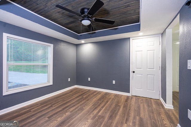 empty room with wooden ceiling, baseboards, a tray ceiling, and wood finished floors