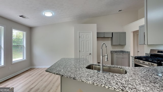 1229 Huntington Place Cir, Lithonia, GA 30058 - kitchen featuring stainless steel gas range, gray cabinets, light stone counters, a sink, and light wood finished floors