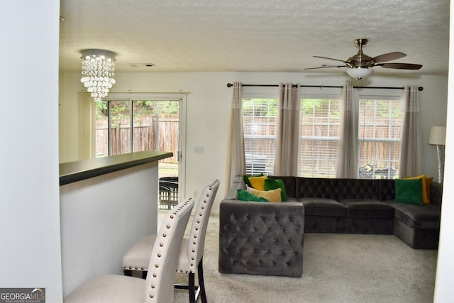 living room featuring carpet floors, a textured ceiling, ceiling fan with notable chandelier, and visible vents
