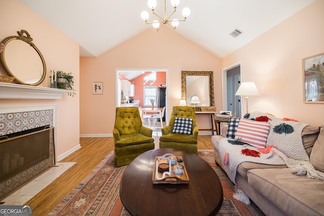 living area featuring a notable chandelier, visible vents, wood finished floors, a tile fireplace, and vaulted ceiling