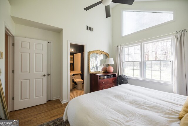 bedroom featuring connected bathroom, a ceiling fan, wood finished floors, a towering ceiling, and visible vents