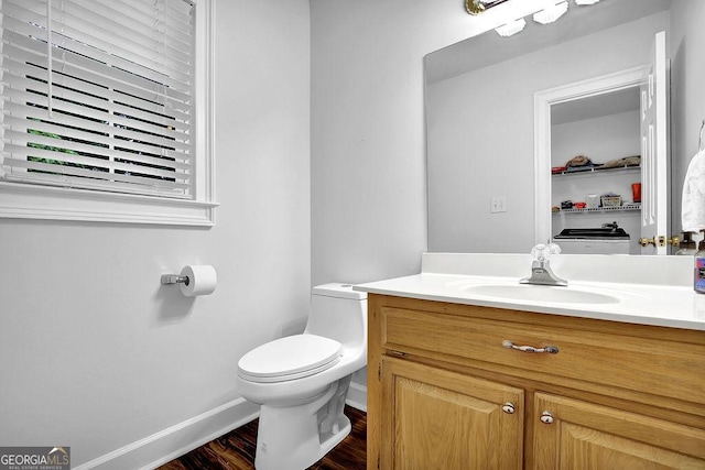 half bath with toilet, baseboards, vanity, and wood finished floors