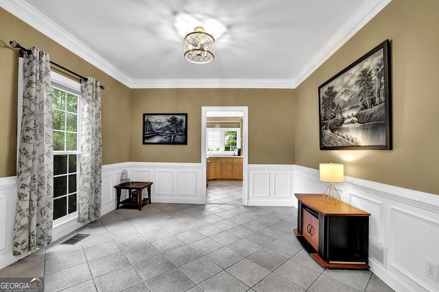 tiled foyer with plenty of natural light, a decorative wall, ornamental molding, wainscoting, and a chandelier
