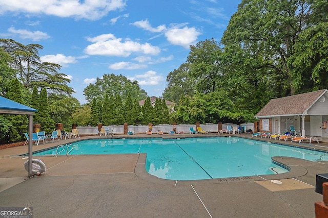 community pool featuring fence, a patio area, and view of wooded area