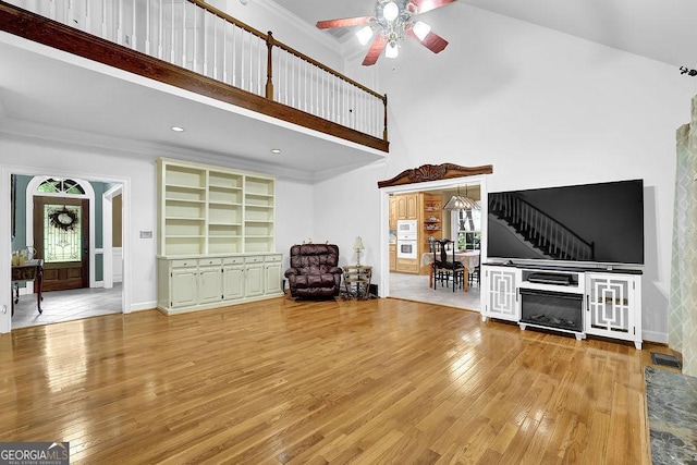 living area with ceiling fan, a high ceiling, hardwood / wood-style floors, crown molding, and baseboards