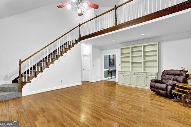 living area featuring stairway, a high ceiling, wood finished floors, ceiling fan, and crown molding
